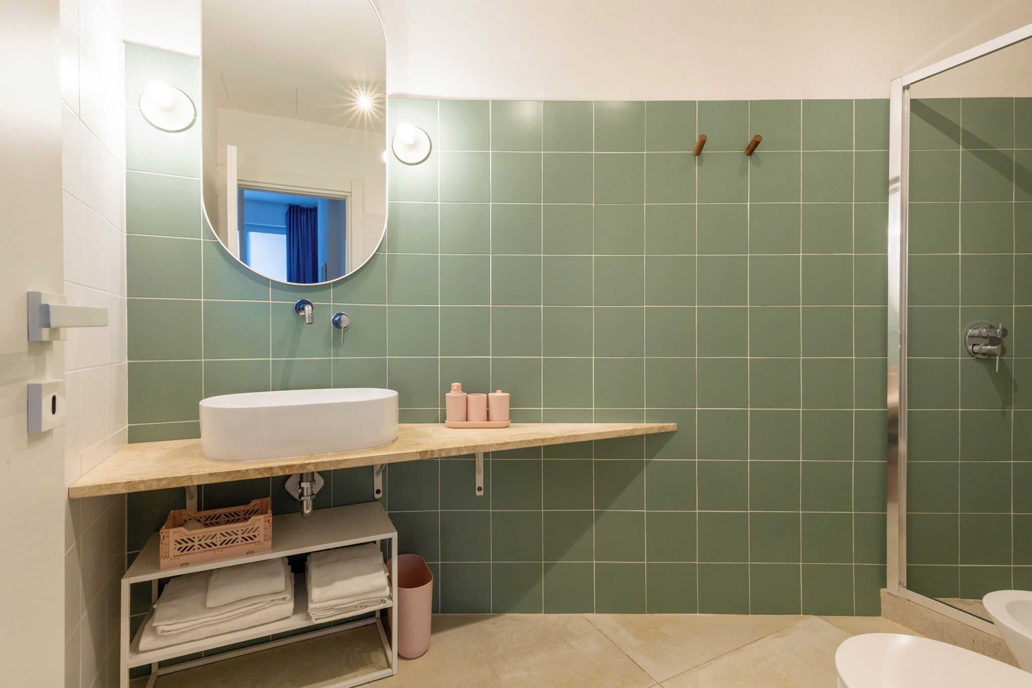 Une salle de bain avec un lavabo blanc, des carreaux verts, un miroir et un espace douche.
