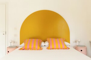 Una cama con dos almohadas, cabecera blanca y un arco amarillo sobre ella.