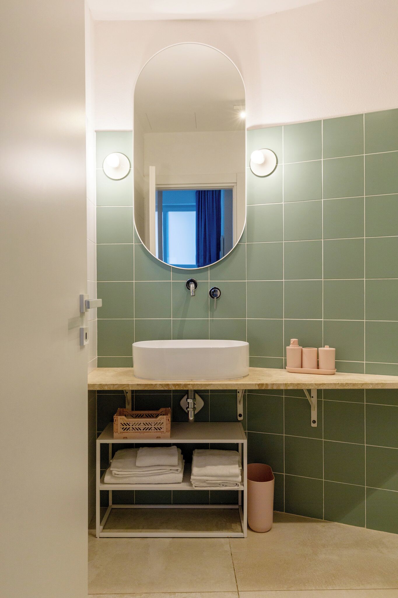 Une salle de bain avec un lavabo blanc, des murs recouverts de carreaux verts et un miroir au-dessus.