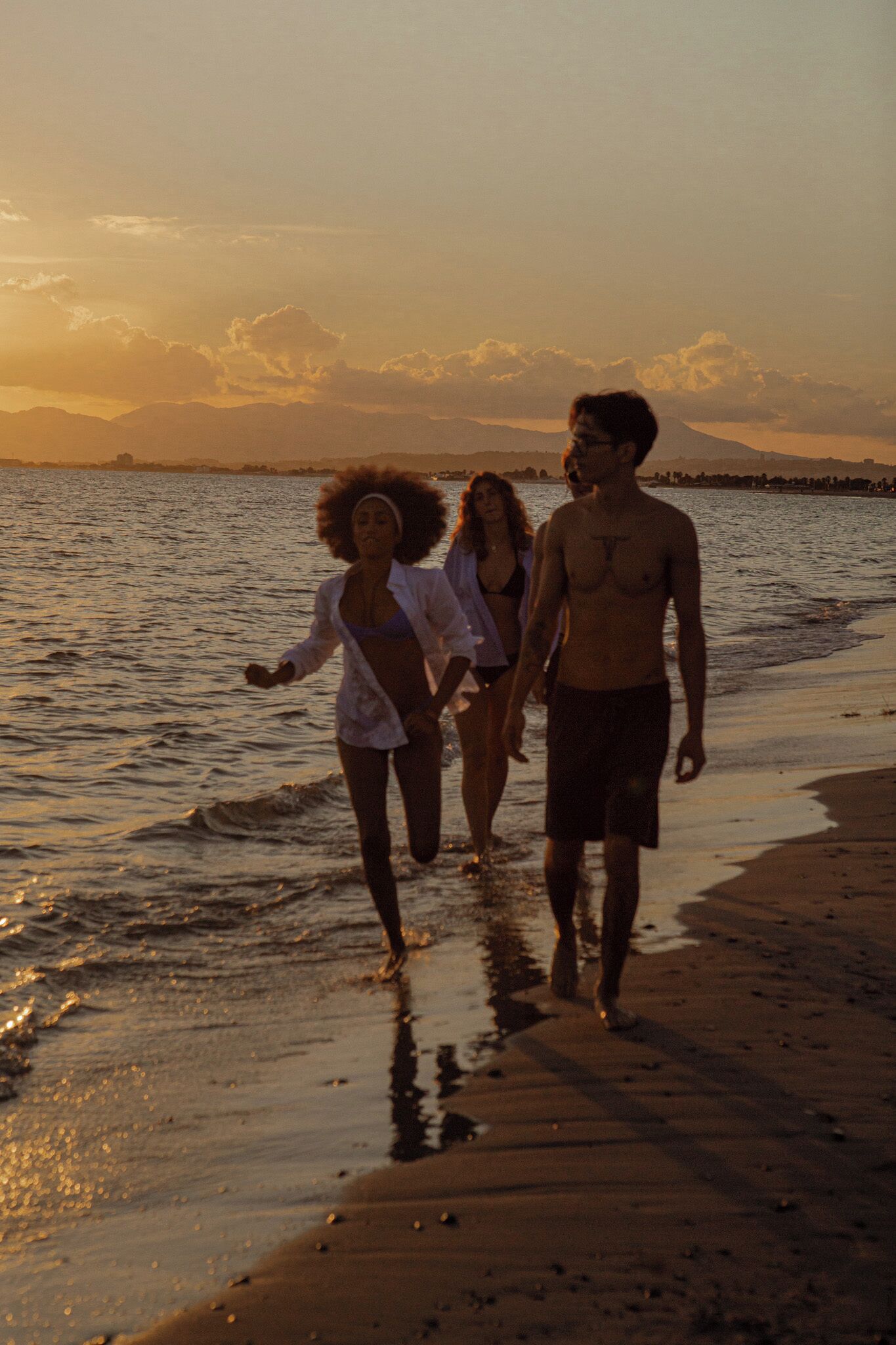 Three people walking on a beach during sunset.
