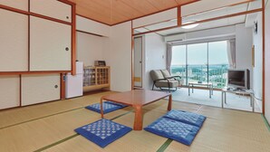 Una habitación japonesa tradicional con esteras de tatami, una mesa de madera baja, un televisor y vistas de la ciudad a través de amplios ventanales.
