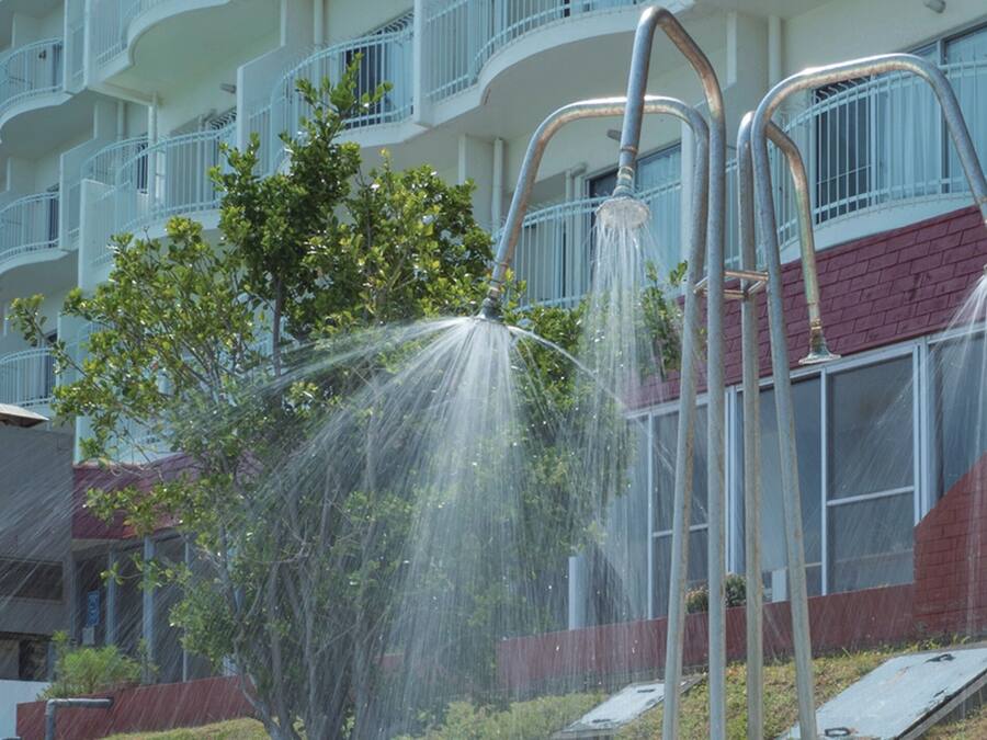 A residential building with multiple balconies, a red brick wall, and a metal structure with water spraying from it.