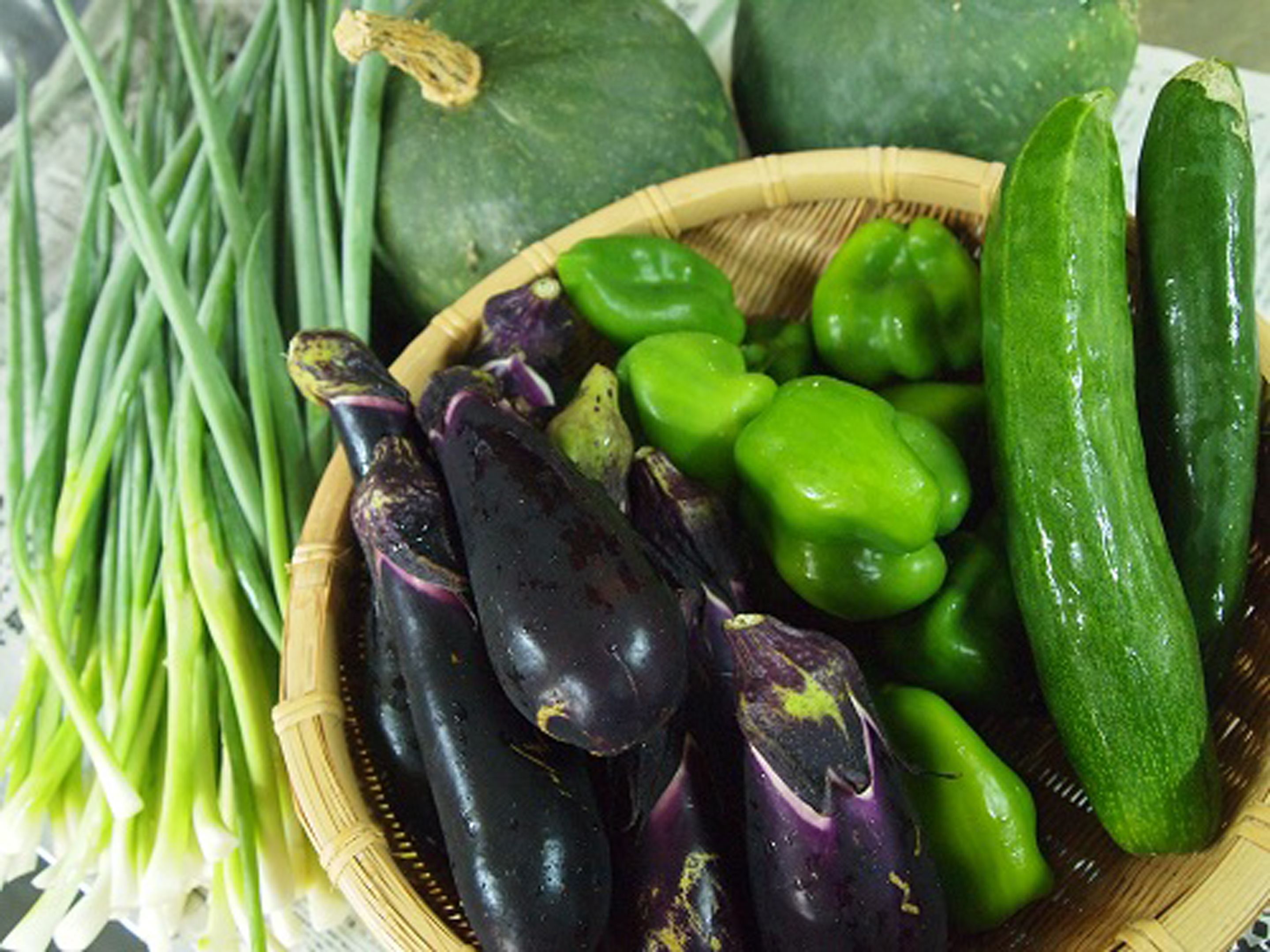 Un panier contenant des poivrons verts, un concombre et des aubergines.