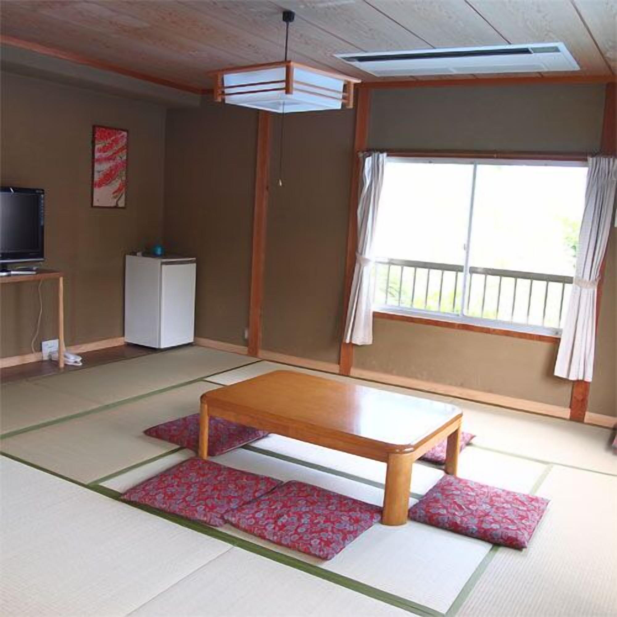 A traditional Japanese room with tatami flooring, a low wooden table, a television, and a sliding door to a balcony.