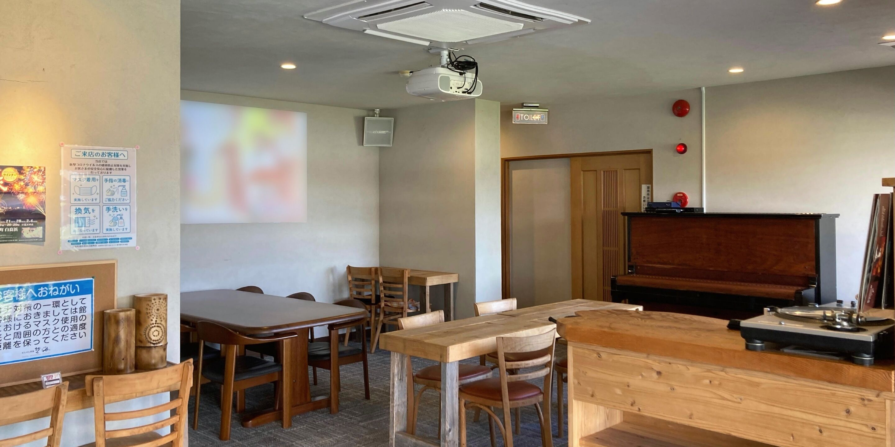 A room with wooden furniture, a projector screen, a piano, and a sign indicating a toilet.