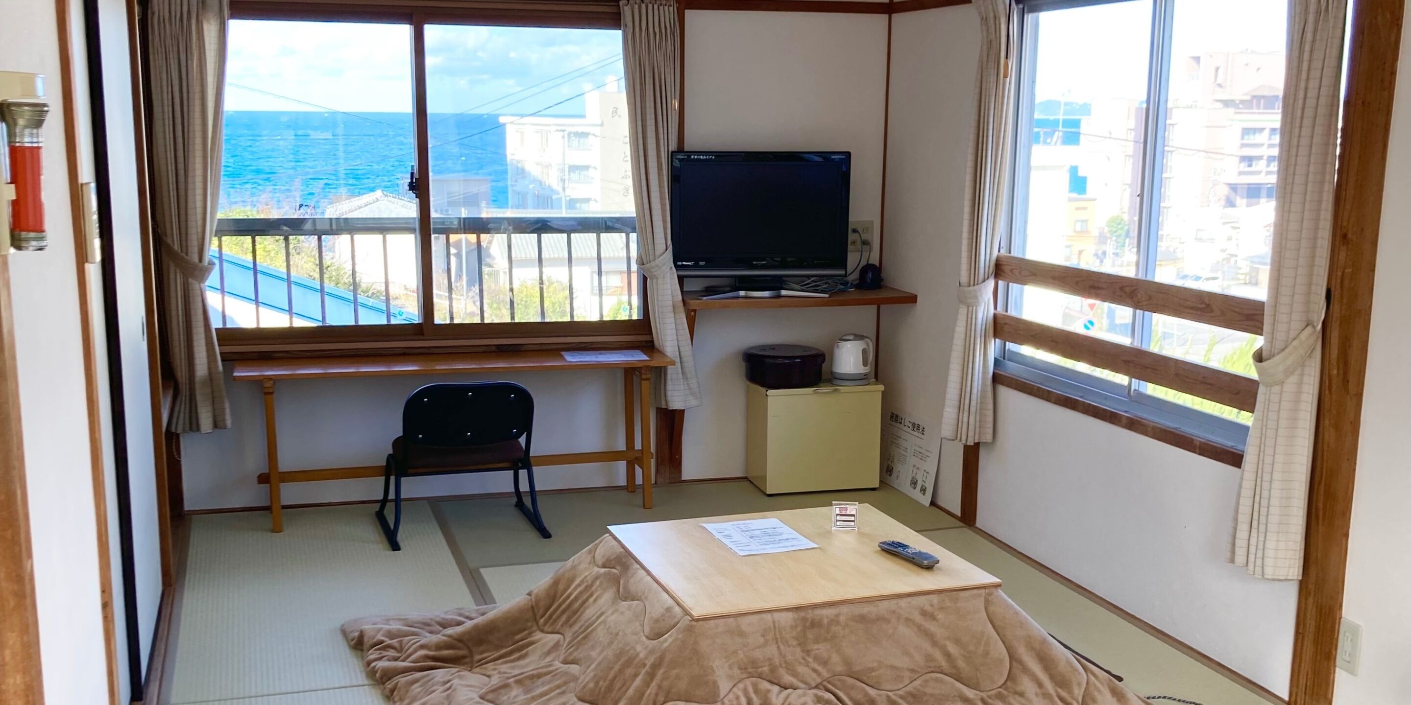 A room with tatami flooring, a television on a shelf, a chair, and a small table with a remote control.