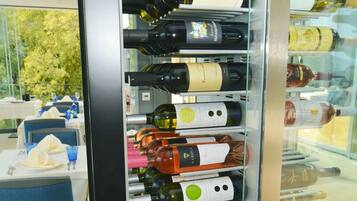 A wine rack with various bottles, a dining area with tables and chairs, and a view of trees outside.