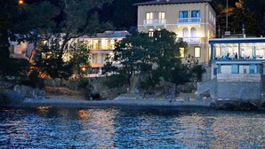 Ein Anwesen am Wasser mit einem mehrstöckigen Gebäude, Balkonen und einem Restaurantbereich mit Außenplätzen.