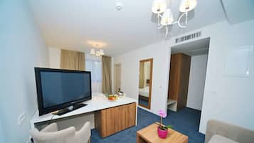 A modern hotel room with a flat-screen TV, a wooden desk, a small coffee table with a potted orchid, a sofa, and a mirror.