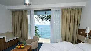 Ein Hotelzimmer mit Bett, Schreibtisch mit Obstschale, Stuhl und Meerblick durch große Fenster.