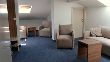 Una habitación con alfombra azul, un sofá, una silla, una mesita de madera y una puerta.