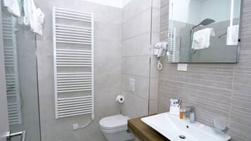 Ein modernes Badezimmer mit Toilette, einer Duschkabine aus Glas, einem Handtuchhalter, einem Waschbecken und einem Spiegel.