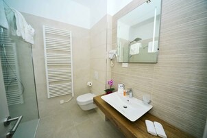 Un baño moderno con cabina de ducha de vidrio, tocador de madera con lavabo blanco y un espejo grande.