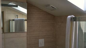 A modern bathroom with a skylight, a sink, a toilet, and a glass shower enclosure.