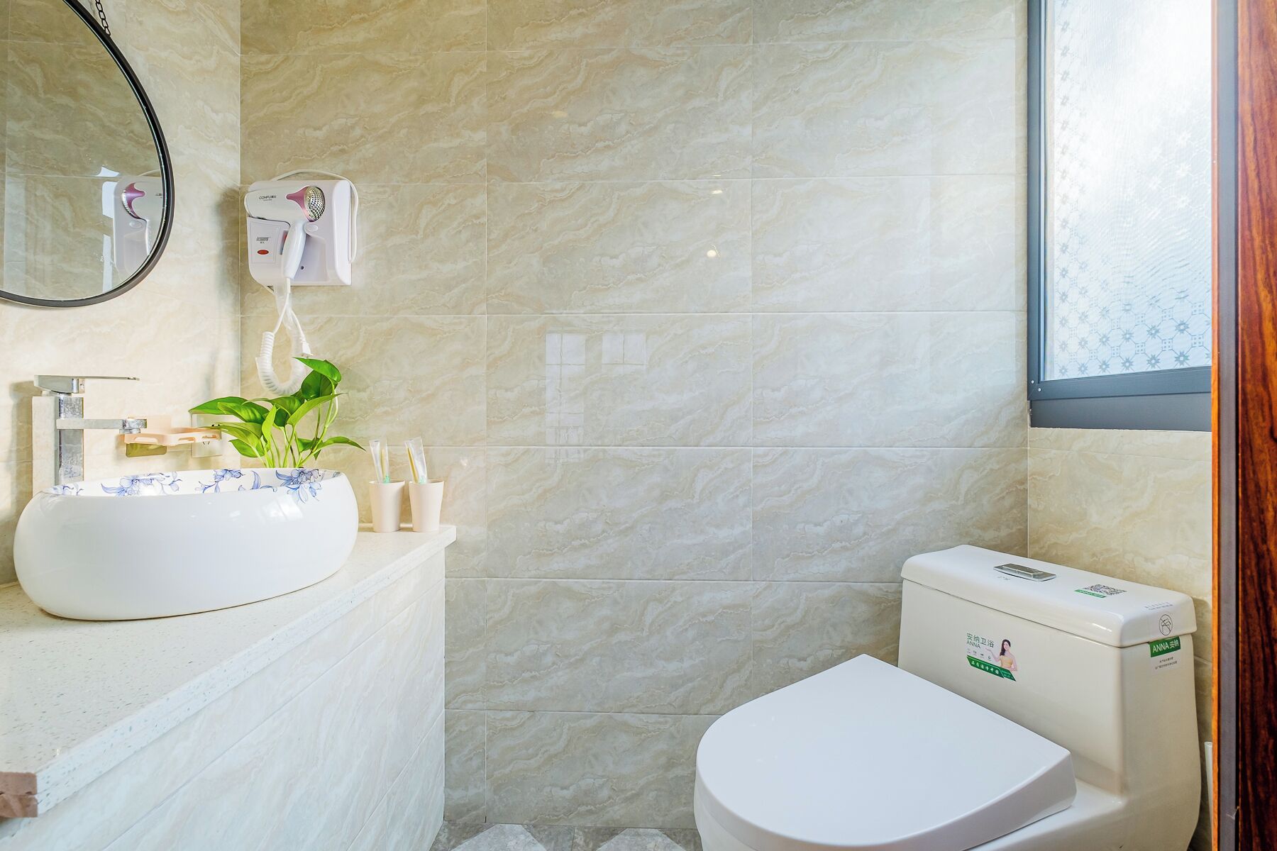 Un baño con suelo de mármol, un lavamanos con una planta, un espejo y un inodoro.