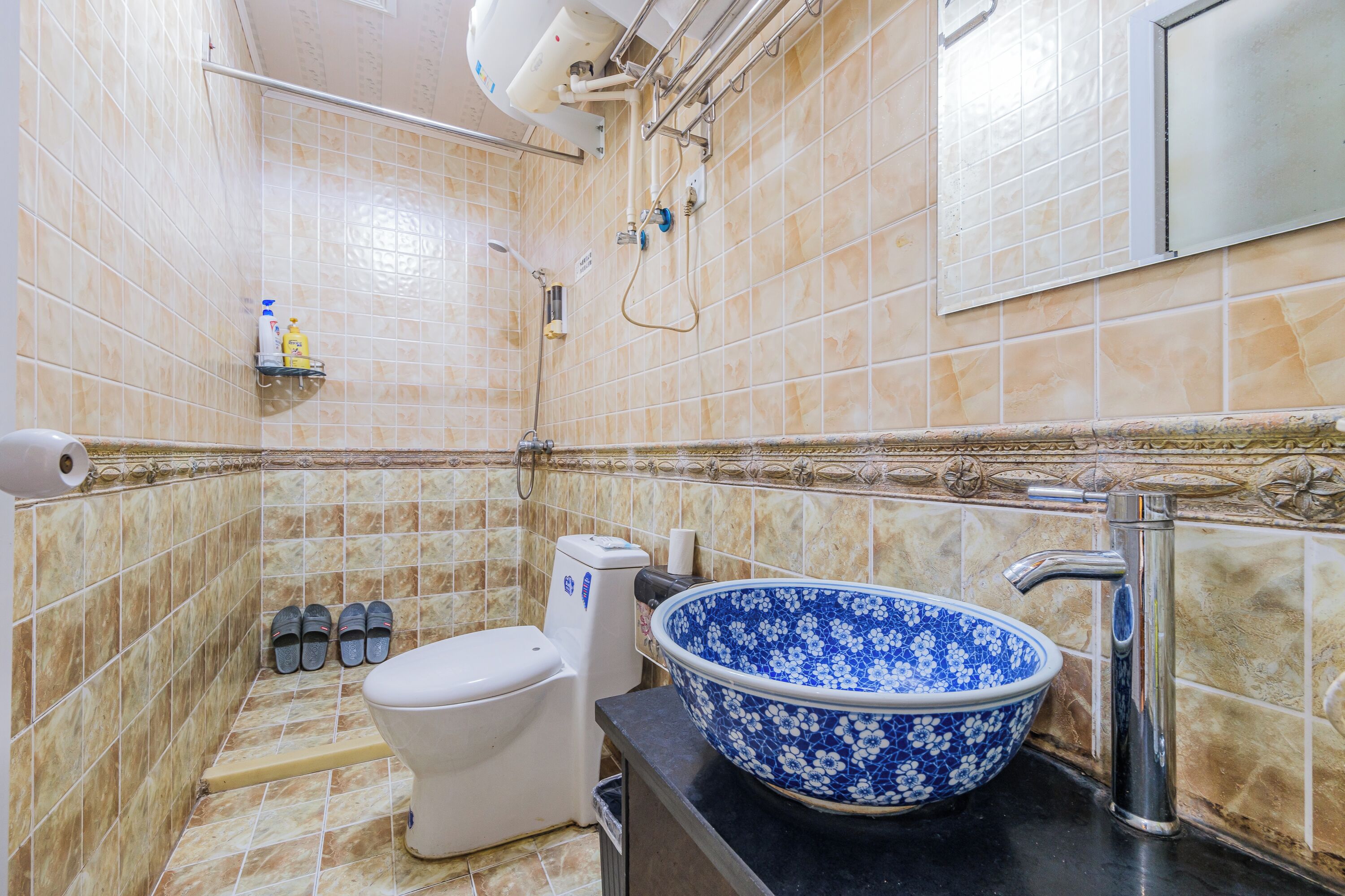 Un baño con inodoro, un lavabo con un lavamanos estampado con motivos florales azules y una zona de ducha con cabezal de ducha de mano.