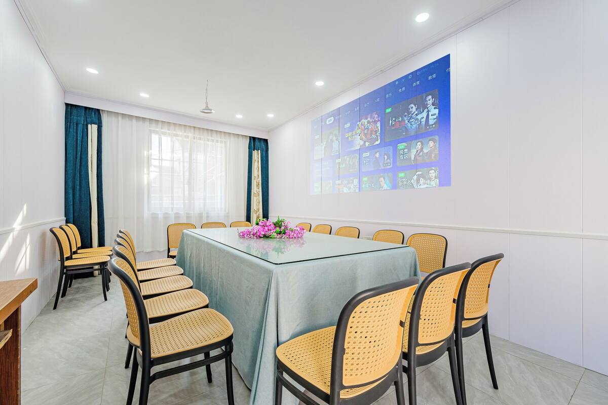 Un salón de conferencias con una mesa de vidrio, sillas de mimbre, un centro de mesa floral y una pantalla de proyección que muestra imágenes.