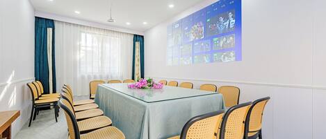 A conference room with a glass table, wicker chairs, a floral centerpiece, and a projection screen displaying images.