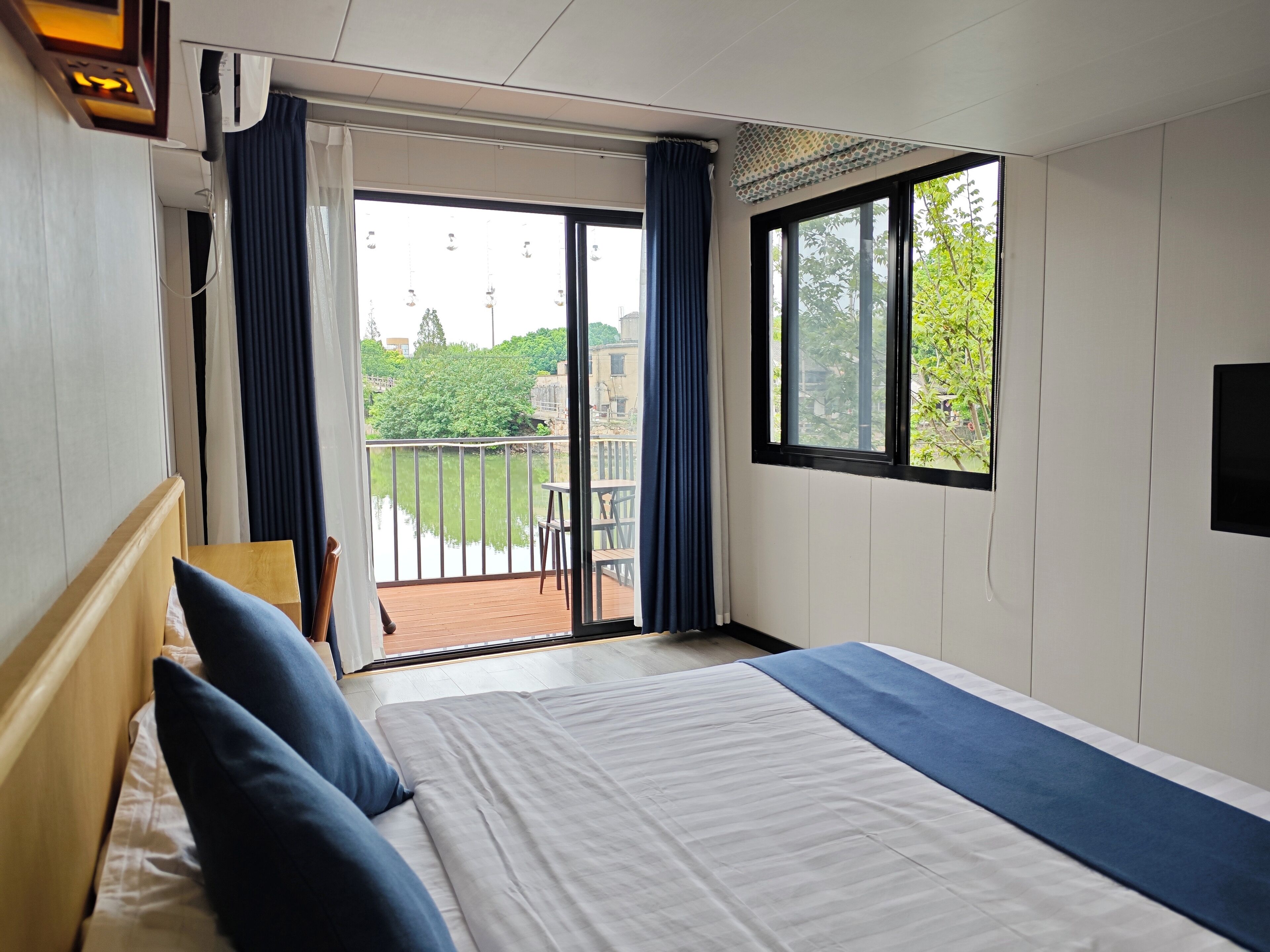A hotel room with a bed, a balcony with a view of greenery, and a window.