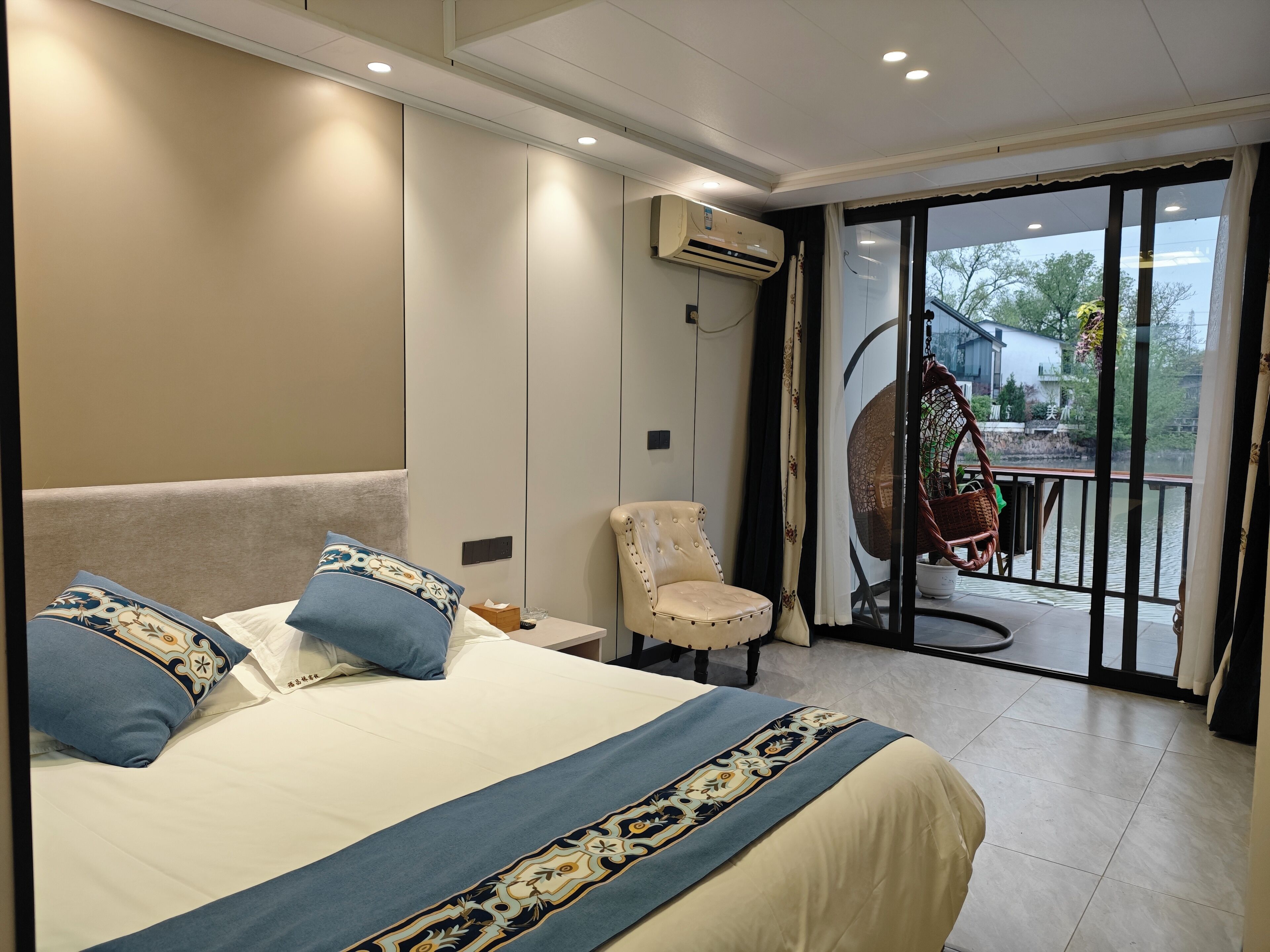 A bedroom with a large bed, a chair, and a view of the outdoors through a glass door.