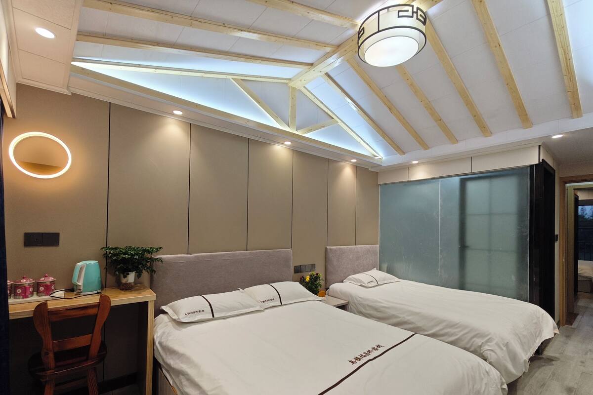 Una habitación de hotel moderna con dos camas, un escritorio, una silla y un ventanal grande.