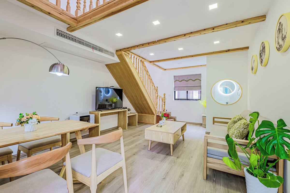 Una habitación amplia con una escalera de madera, un comedor con muebles de madera y un televisor.