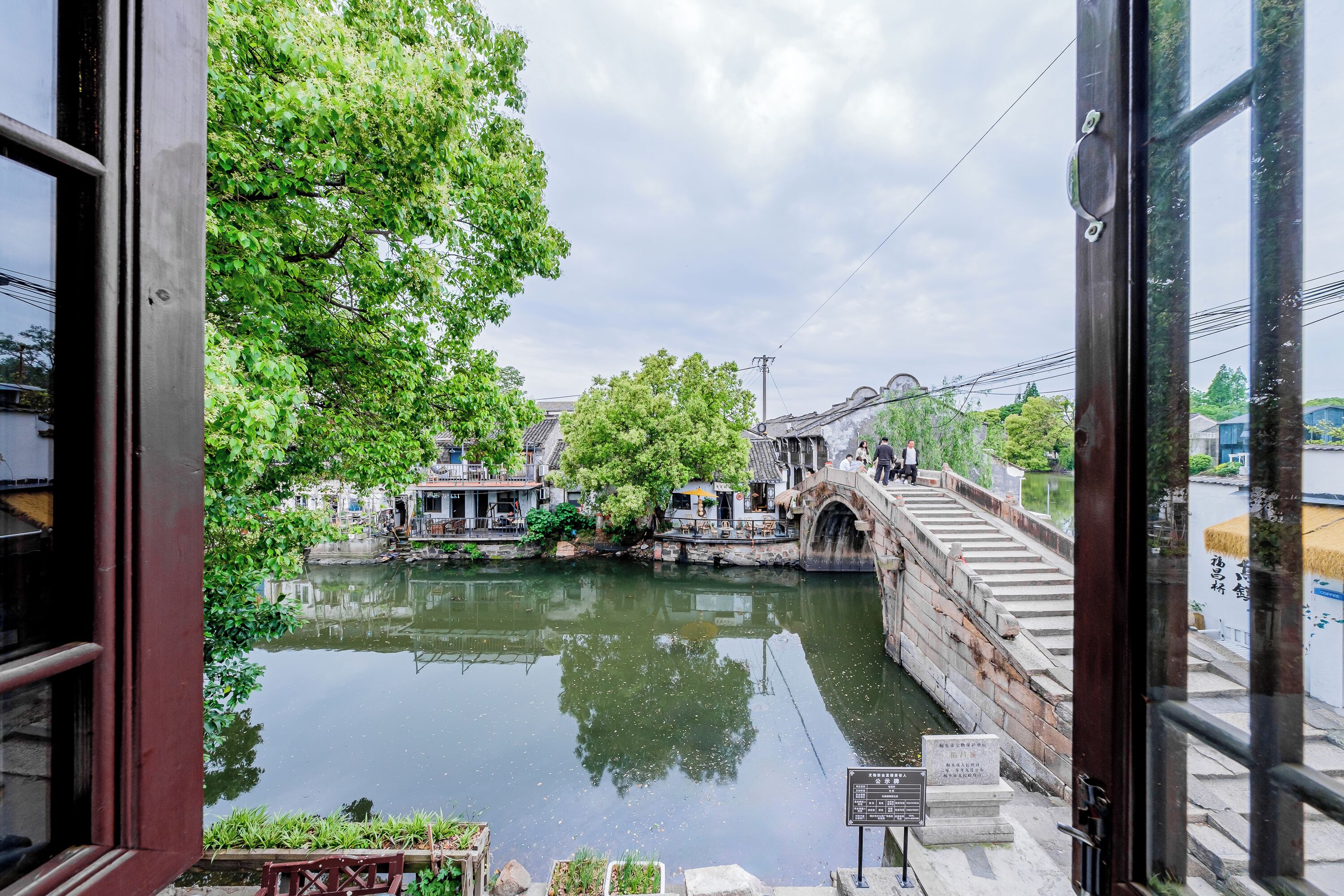 Un puente tradicional sobre un río tranquilo, con edificios y árboles al fondo.