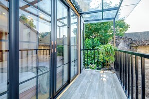 A modern balcony with large glass doors, a wooden floor, and a view of a garden and traditional architecture. - Wuzhen Fuchang Bridge Inn (Jiaxing)