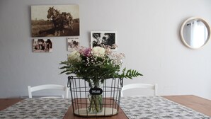 Una mesa de comedor con una cesta de mimbre que contiene un ramo de flores, una fotografía antigua y un espejo en la pared.