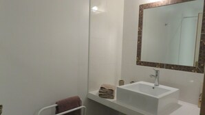 Un baño con un lavabo blanco, un espejo con marco decorativo, un perchero con toallas y un dispensador de papel higiénico.