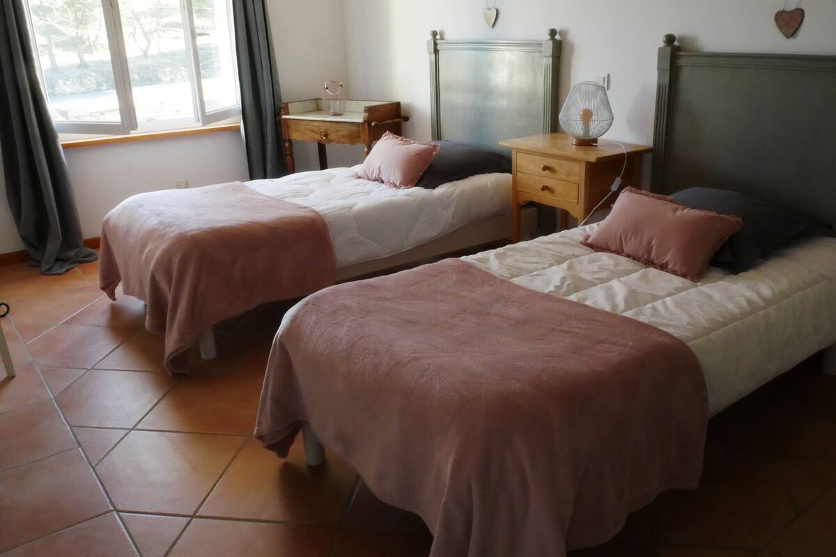 A bedroom with two beds, a nightstand, a dresser, and a window with curtains.