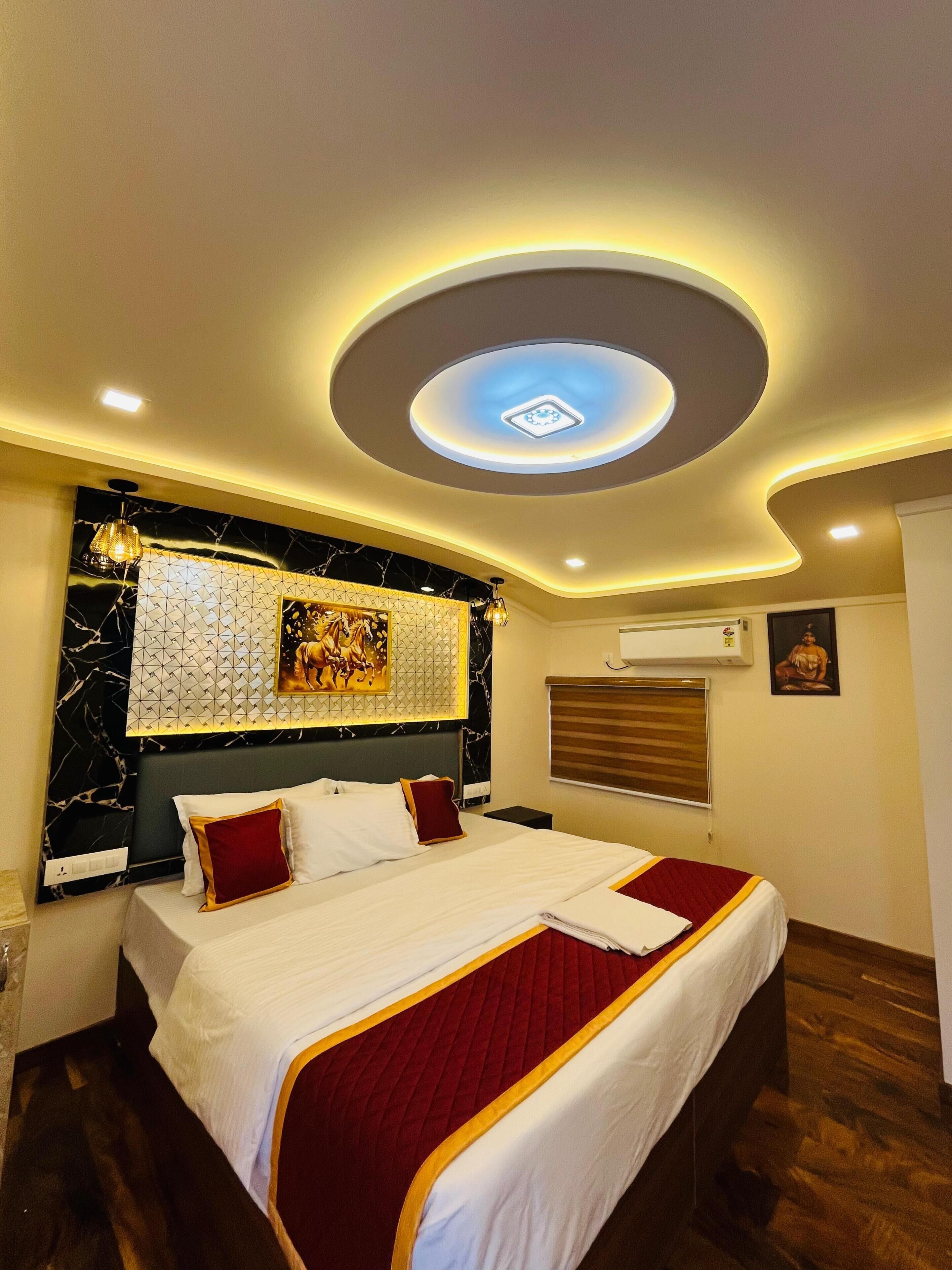 A hotel room with a bed, a ceiling light, a wall-mounted air conditioner, and a window with blinds.
