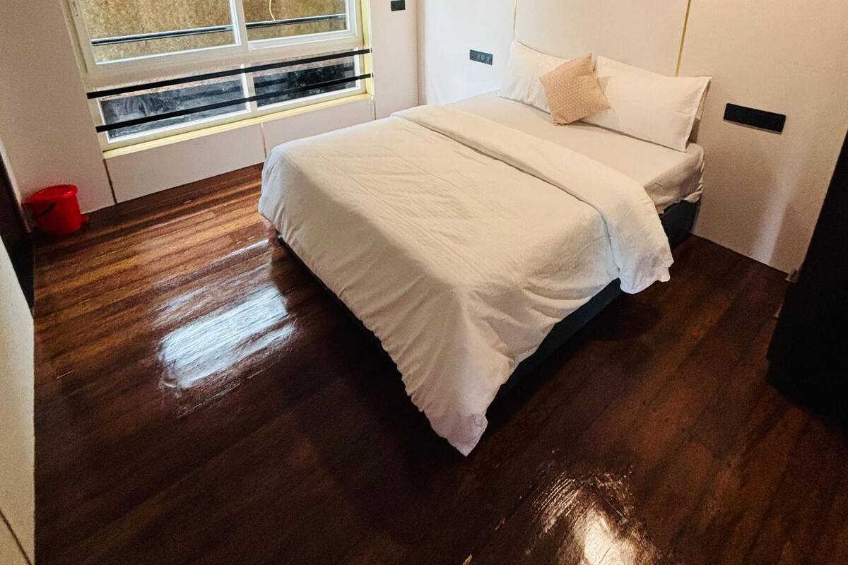 A bedroom with a bed, a window, and a red bucket on the floor.