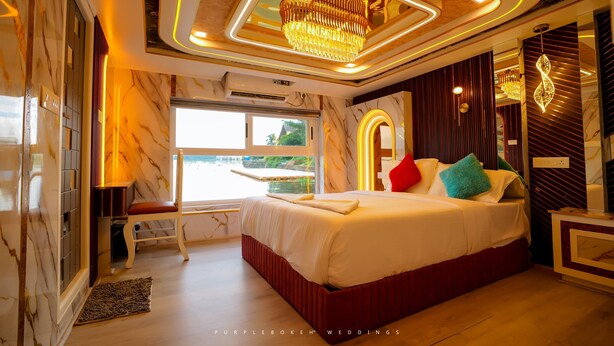 A modern bedroom with a large bed, a chandelier, and a view of the outdoors. - Beachparadise  Daycruise houseboat (Ambalapuzha)