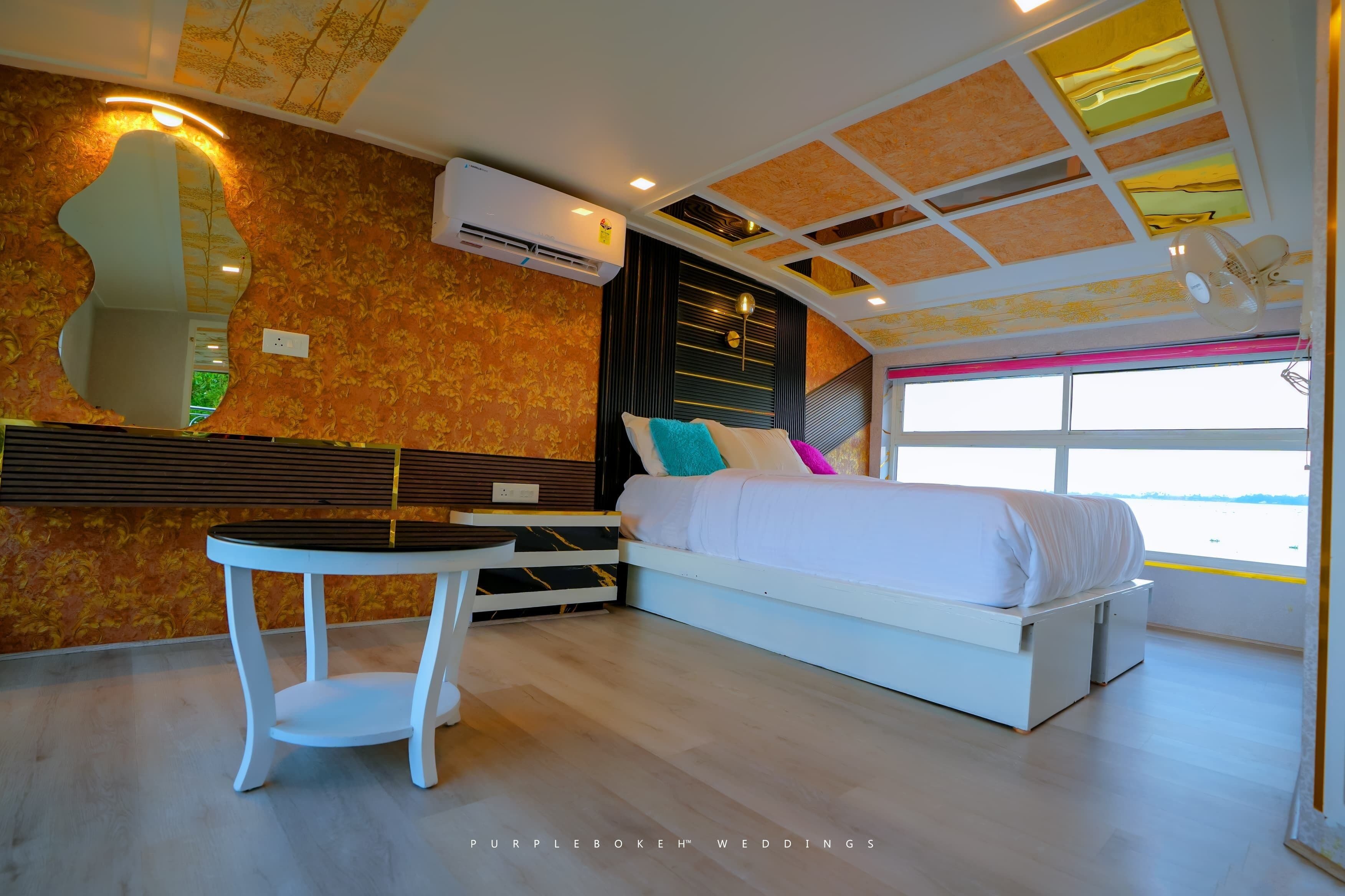 Un dormitorio moderno con cama, mesitas de noche, una mesa redonda y un ventanal grande.