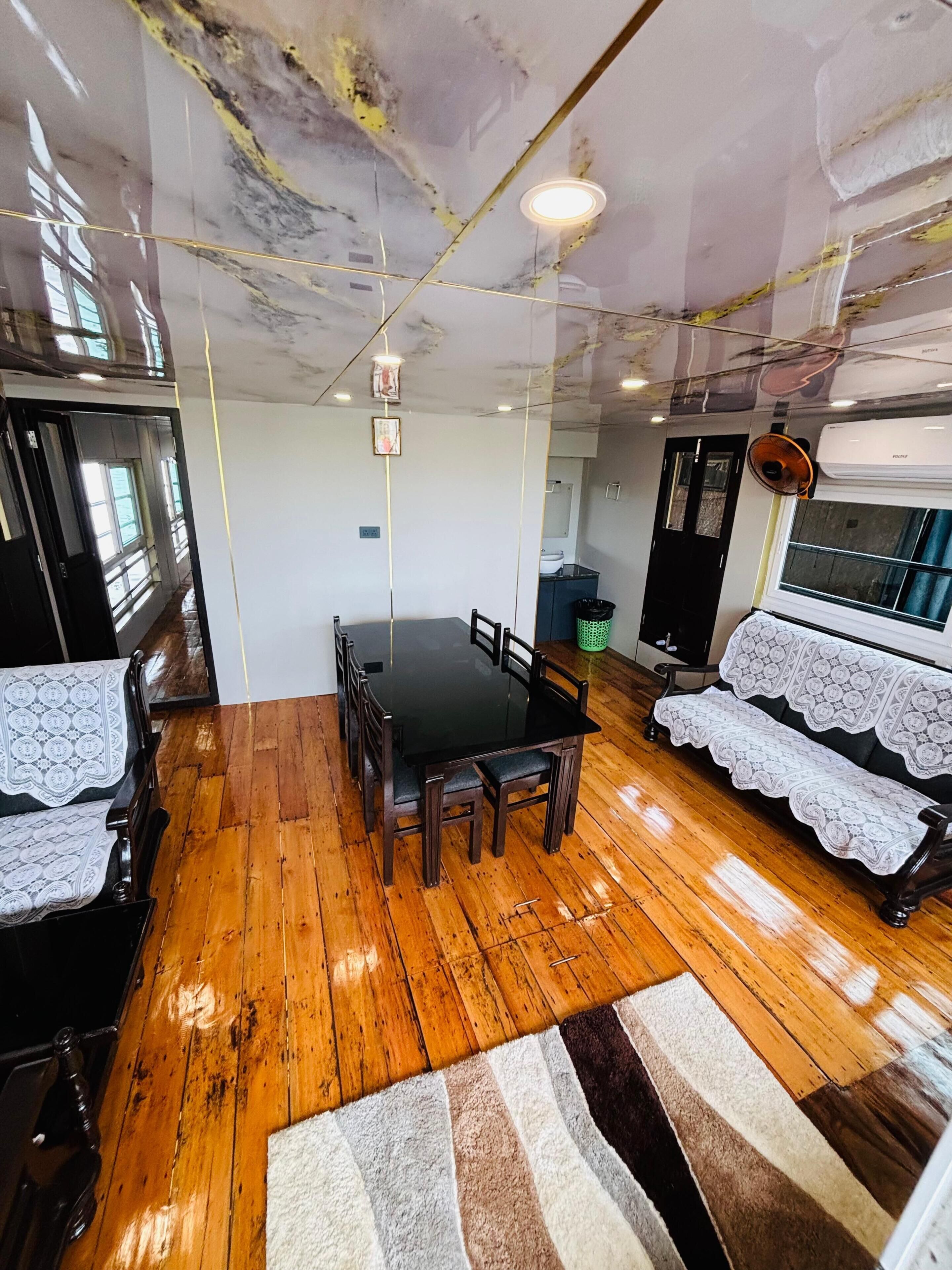 Ein Zimmer mit Holzboden, einem Esstisch mit Stühlen, einem Sofa mit Spitzenüberwurf und einem Deckenventilator.