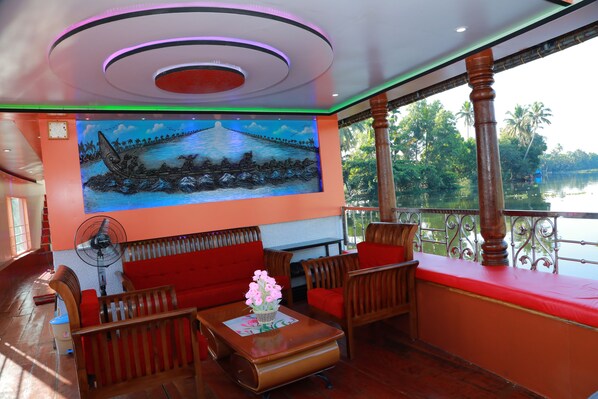 A room with a mural of a river scene, wooden furniture, a fan, and a view of a lake.
