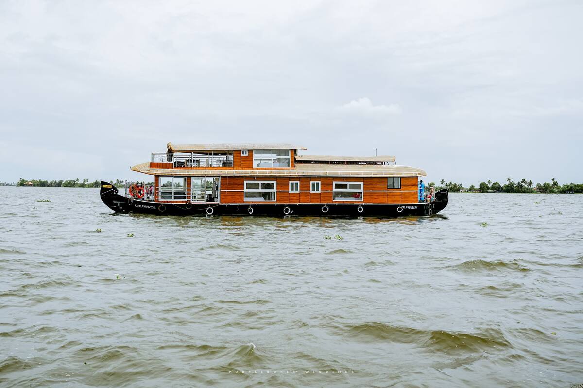 A multi-deck houseboat with a wooden exterior, large windows, and a flat roof.