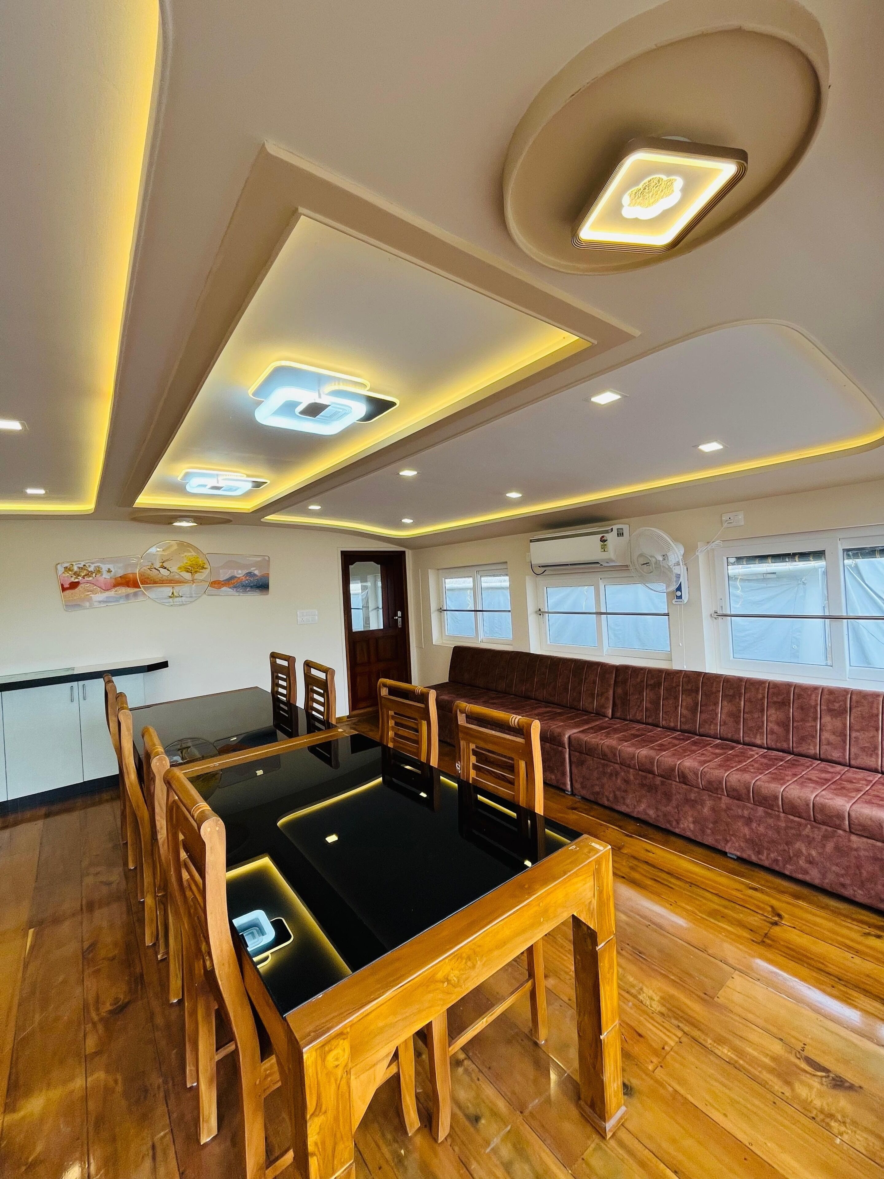 Un intérieur moderne comprenant une table à manger, des chaises en bois, un canapé et un plafond doté d’un éclairage encastré.