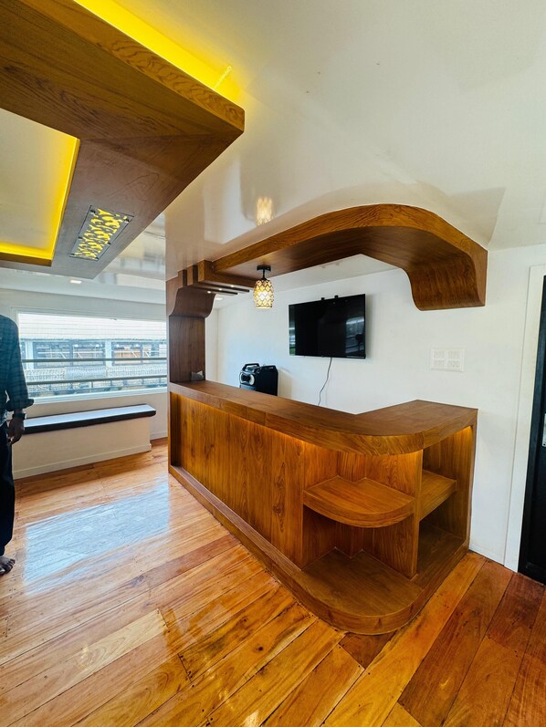 Un mostrador de recepción de madera con un banco integrado, un televisor de pantalla plana montado en la pared y una ventana con vistas a un balcón.