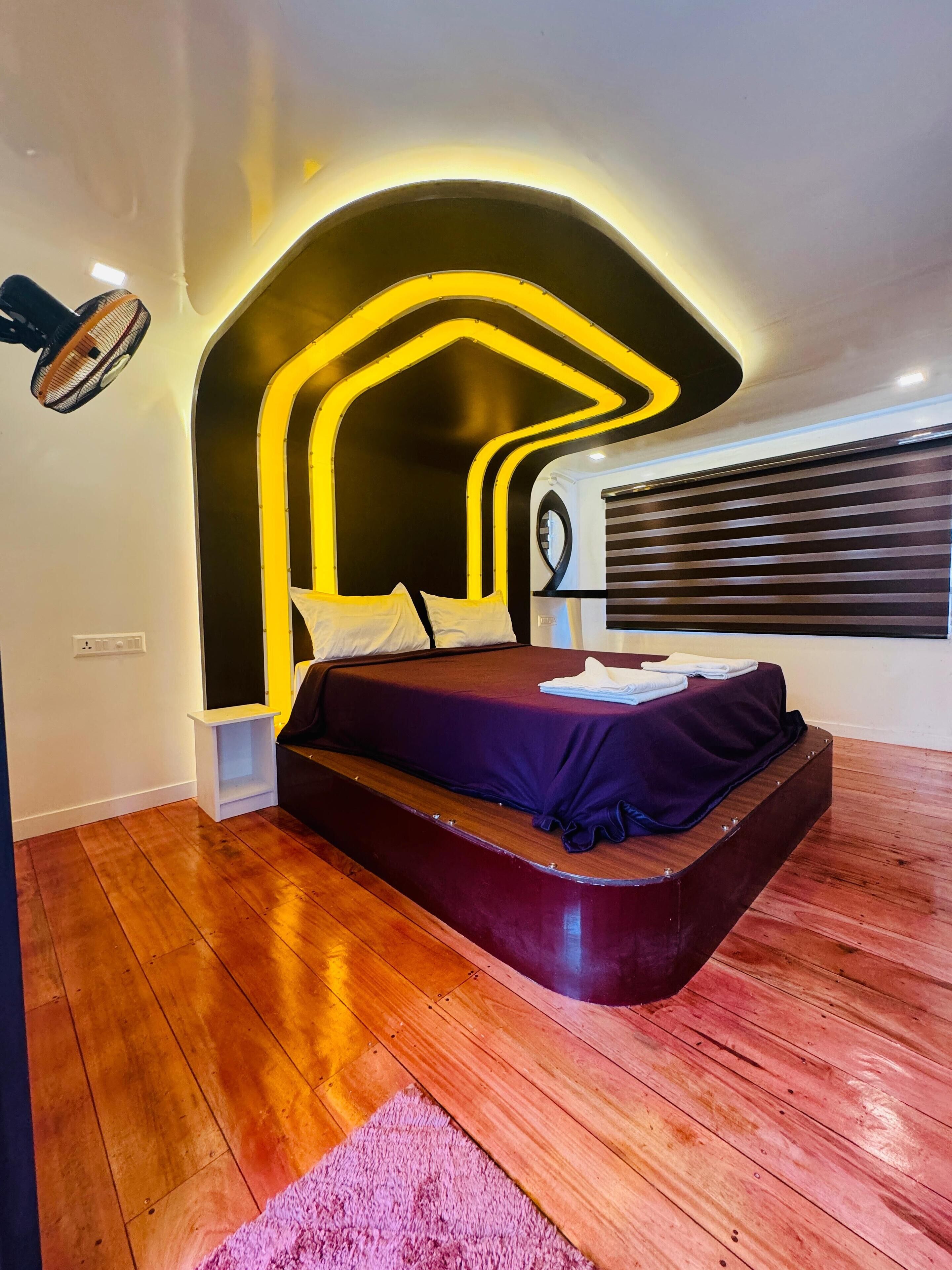 A modern bedroom with a curved headboard, a wooden floor, and a bed with a purple bedspread.