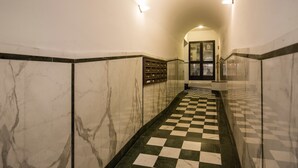 A hallway with checkered flooring, marble walls, and a glass door at the end.