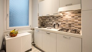 A modern kitchen with white cabinets, a tiled backsplash, a window, and a fruit bowl on the counter.