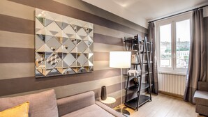 Een moderne woonkamer met een gestreepte wand, een geometrische spiegel, een vloerlamp, een boekenkast en een bank.