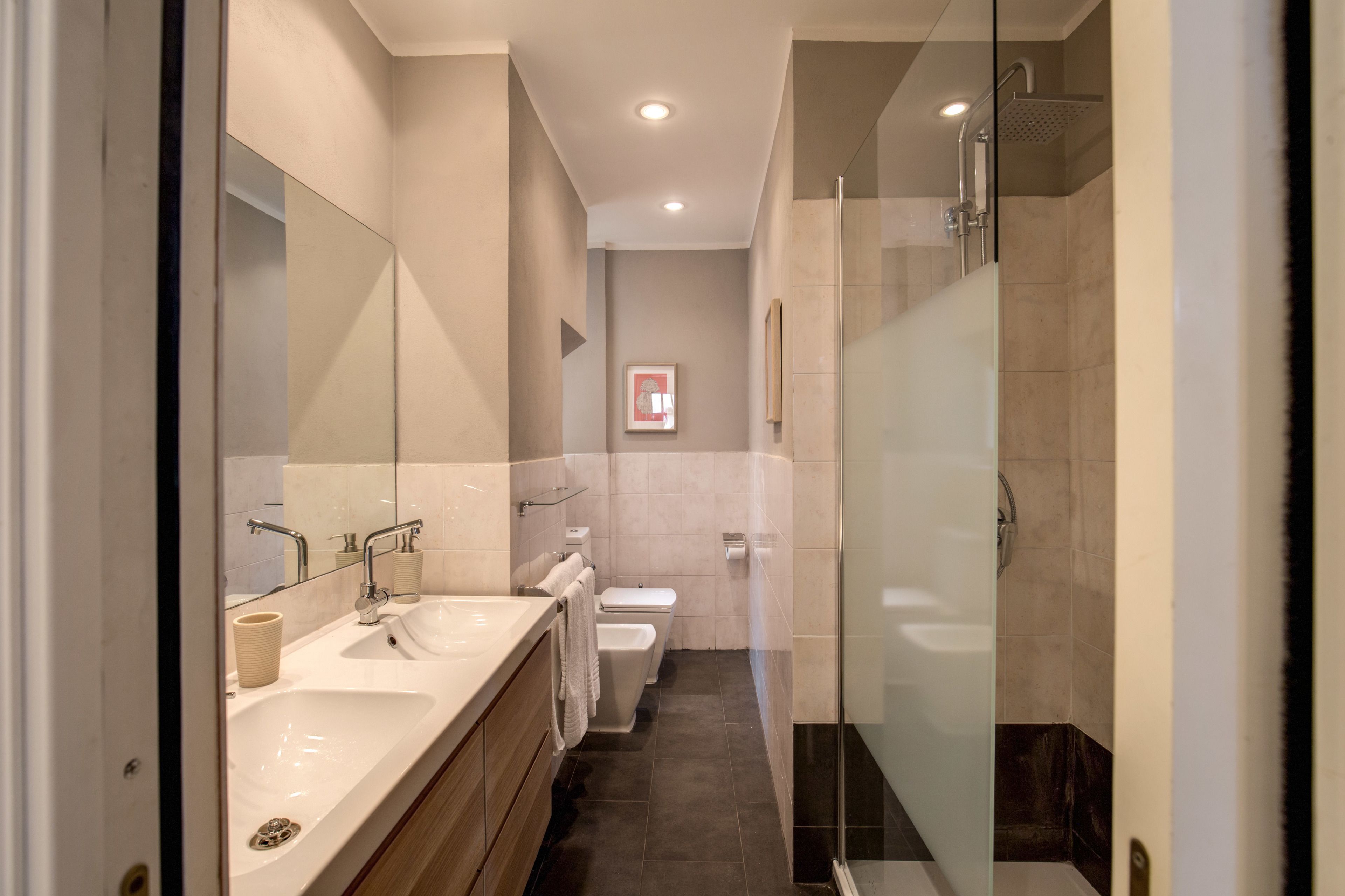 A modern bathroom with a double sink, toilet, and shower area.