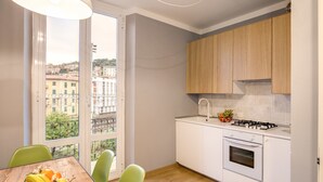 Een moderne keuken met witte kastjes, een gasfornuis en stadszicht door grote ramen.
