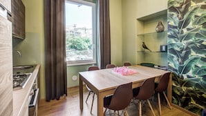 Une cuisine de taille réduite avec une fenêtre, une table à manger avec des chaises et une étagère ornée d’objets décoratifs.