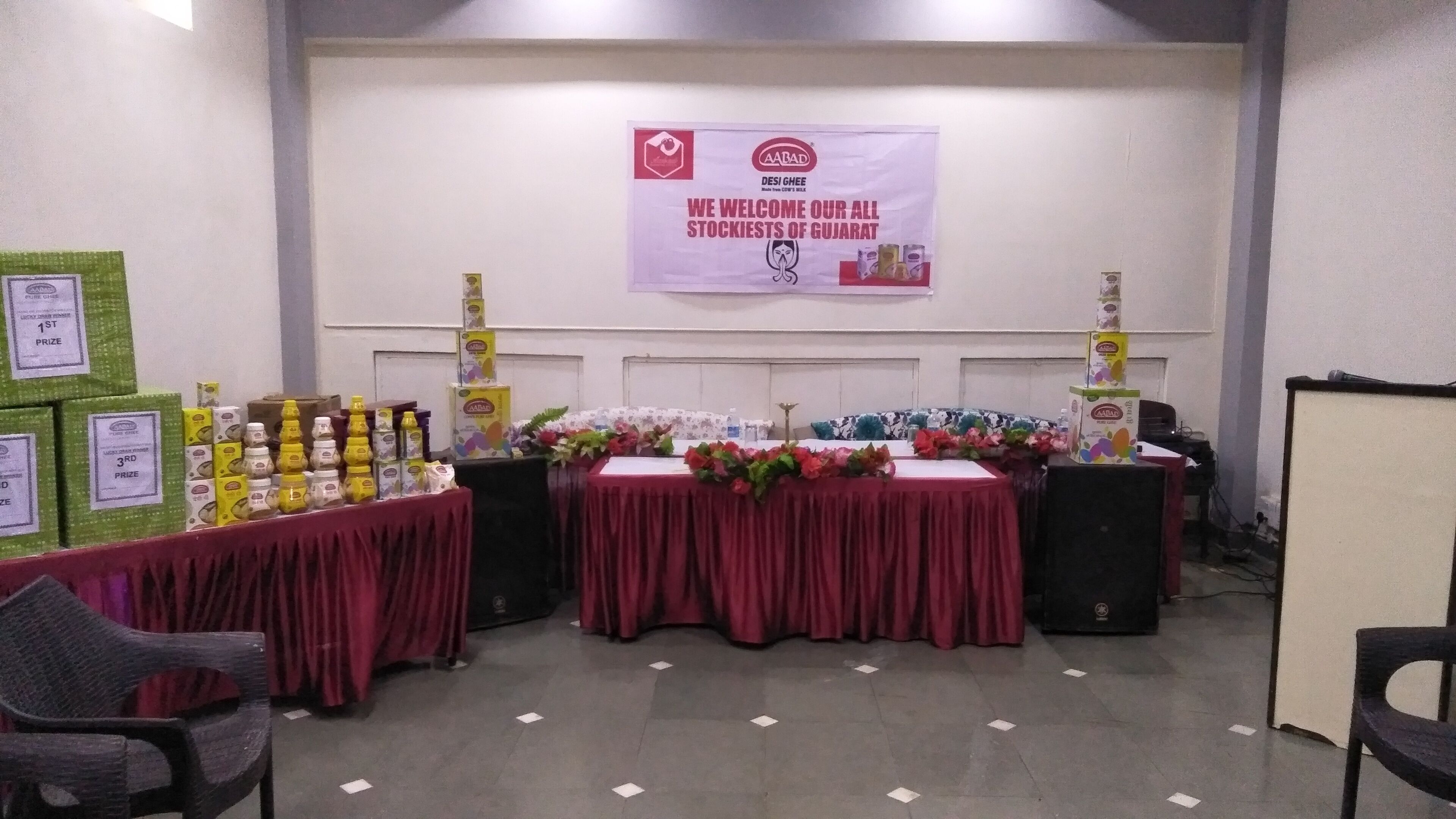 Ett konferensrum med en banderoll där alla återförsäljare från Gujarat välkomnas, bord med produkter och en talarstol.