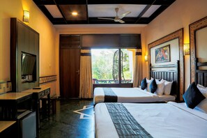 A hotel room with two beds, a desk, a television, and a view of greenery outside. - Hotel Mount Regency (Abu Road)