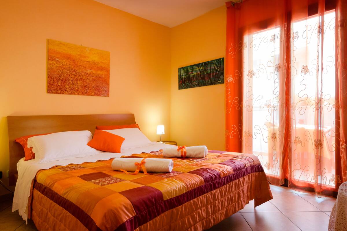 A hotel room with a bed, two bedside tables, a nightstand, and a window with curtains.